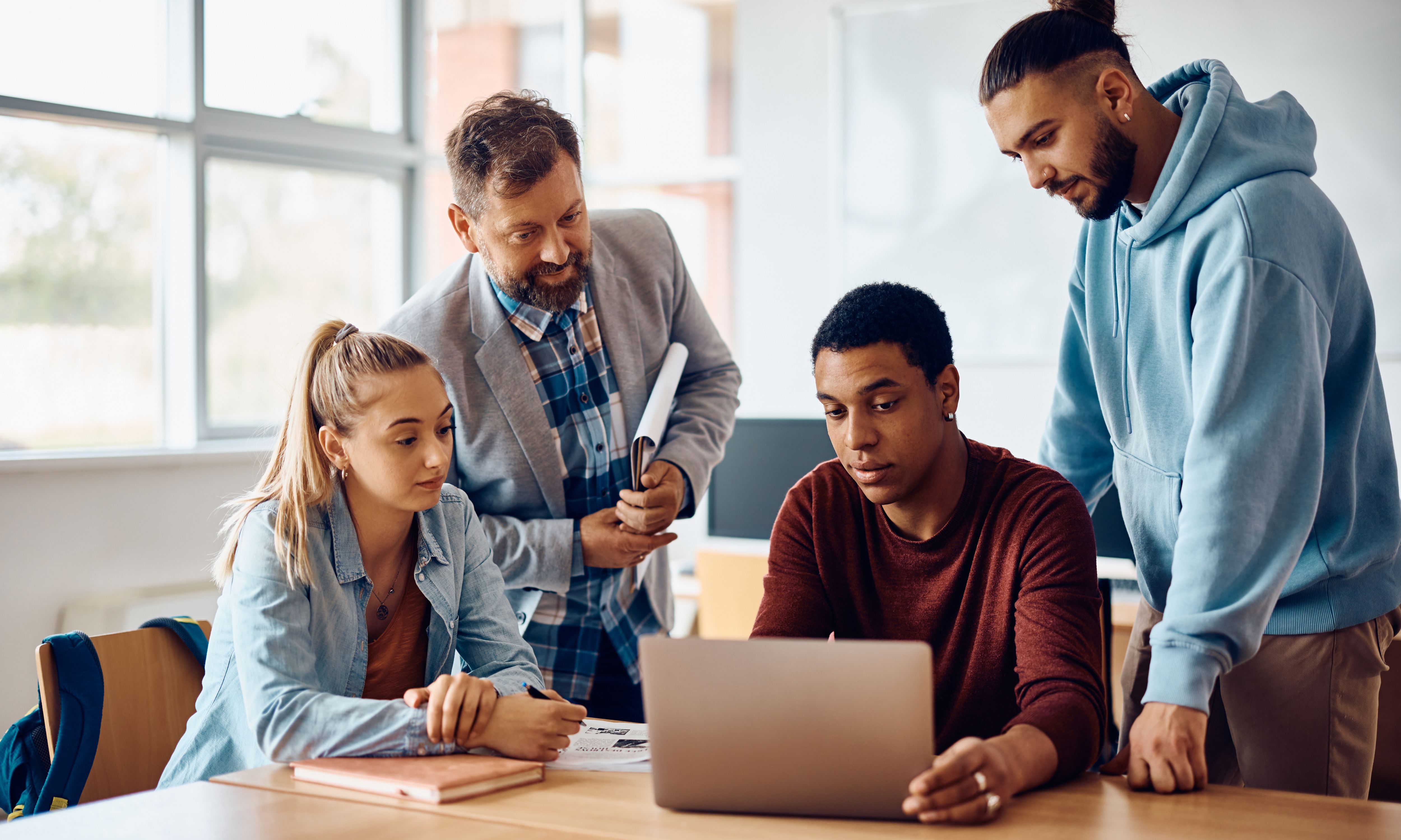 Group of learners gathered around a laptop with older man teaching them