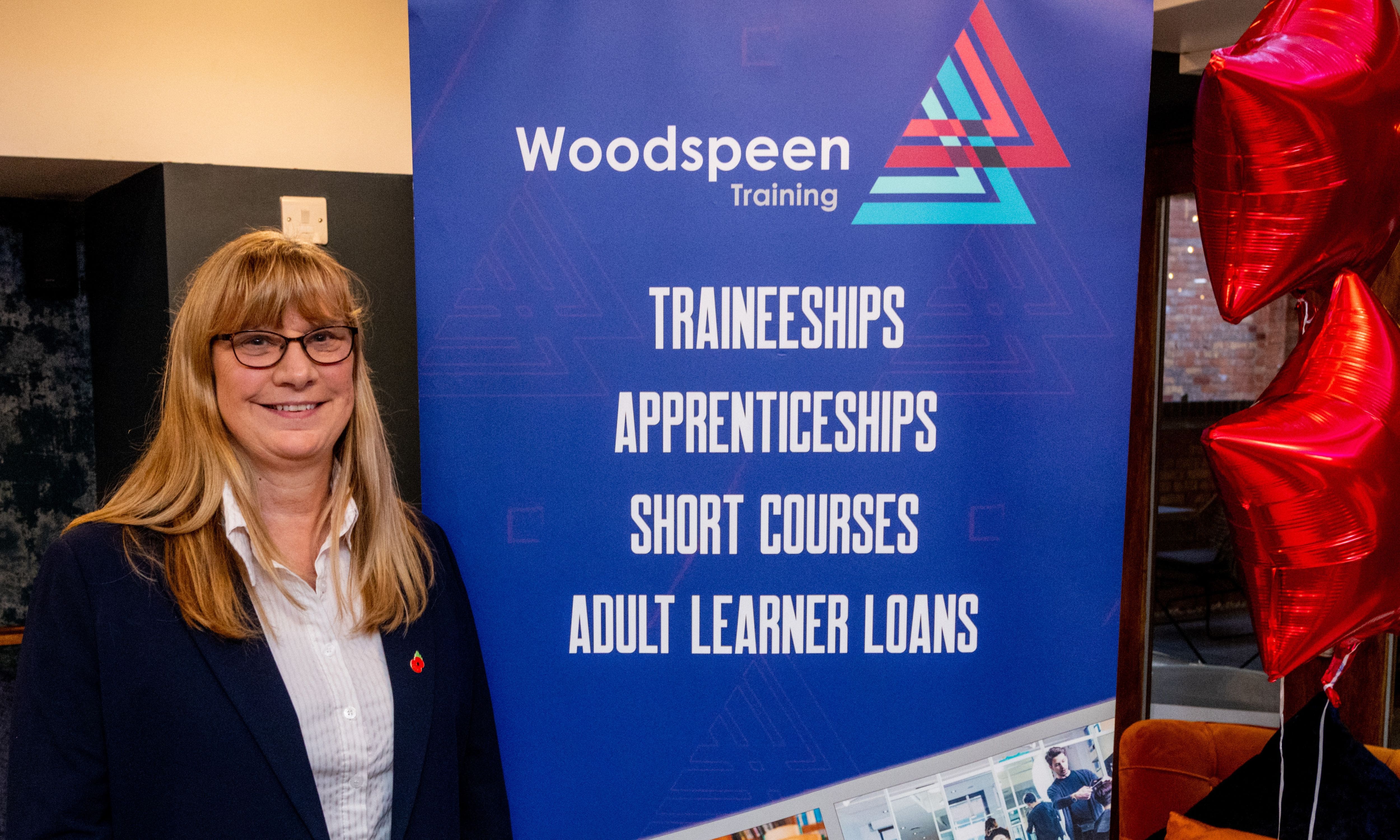 Samantha Wilson standing next to Woodspeen Training banner with red star balloons